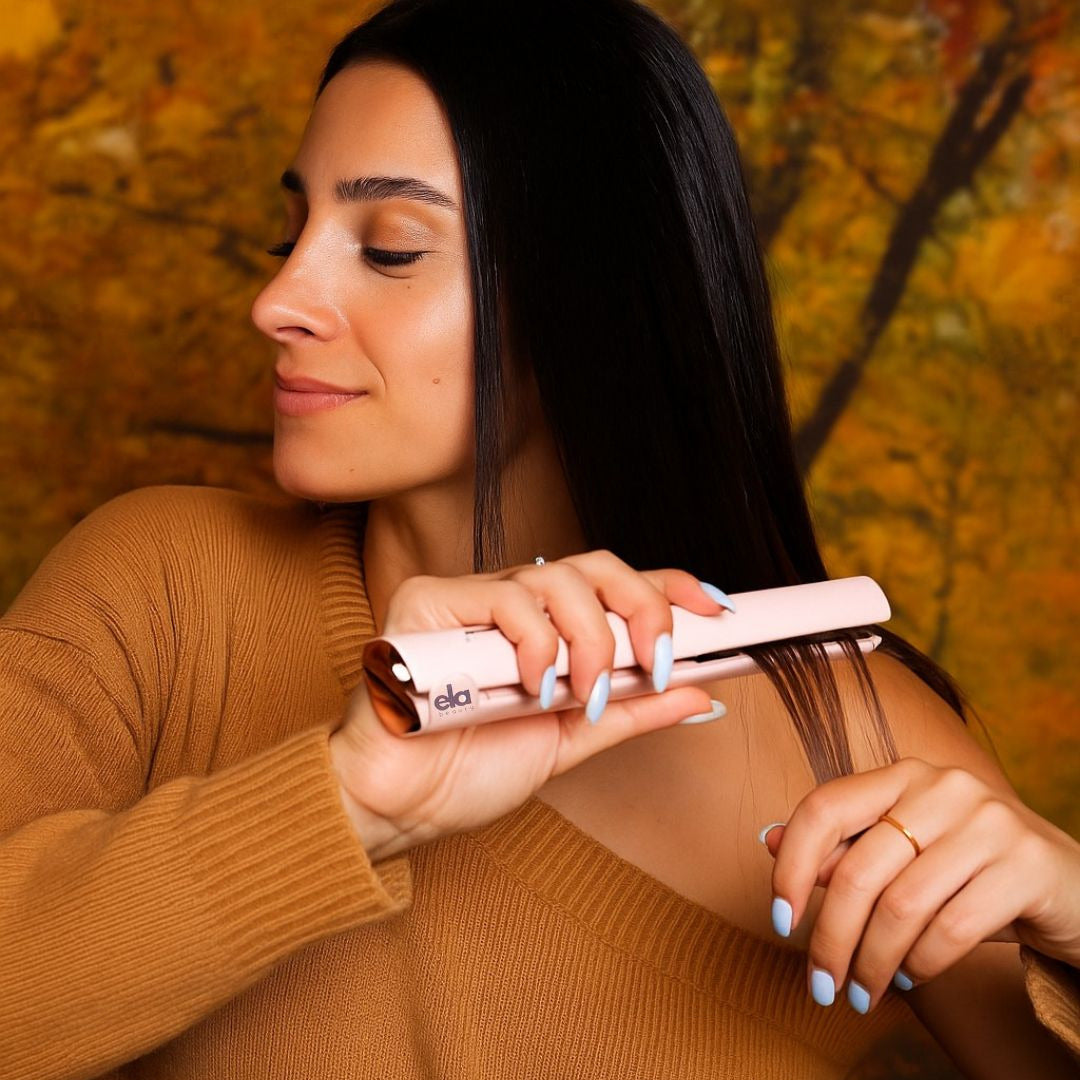 Woman using a hair straightener with a blurred autumn background